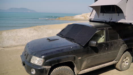 Portable-solar-photovoltaic-panel,-charging-battery-of-a-4×4-by-the-sea-on-an-Off-Road-Adventure-Travel-in-Albania