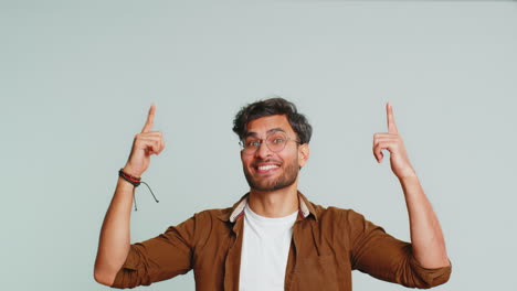 Young-man-showing-thumbs-up-and-pointing-overhead-on-blank-space-place-for-your-advertisement-logo