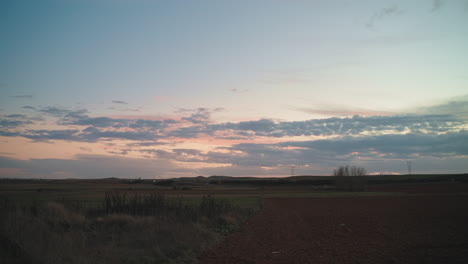 Vast-rural-field-under-a-cloud-filled-dusk-sky-with-a-motorway-nearby