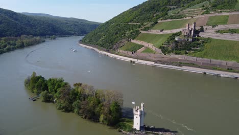 Barge-ship-cruising-on-river-Rhine-Valley-between-Mouse-tower-in-Bingen-and-Burg-Ehrenfels-Castle-in-Ruedesheim,-Germany