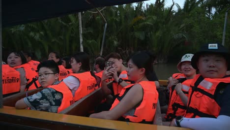 A-group-of-tourists-on-a-boat-ride-at-Amphawa-Floating-Market-did-a-short-stop-in-the-middle-of-the-canal-to-take-some-photos,-waved-at-the-tourists-on-the-other-boat-on-their-way-to-the-river