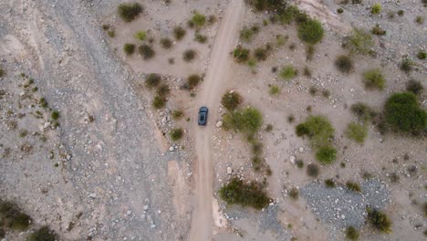 Top-down-drone-shot-following-a-grey-car-driving-on-an-unpaved-road-through-the-Tatón-desert-in-Catamarca,-Argentina