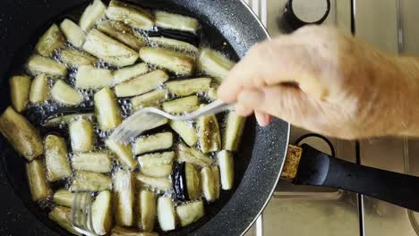 Male-hands-mixing-frying-eggplant-with-forks-in-vegetable-oil