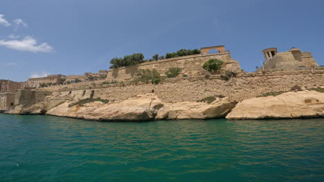 Una-Toma-Suave-De-Un-Edificio-Antiguo-A-Lo-Largo-De-La-Costa-De-Malta-Y-El-Mar-Turquesa