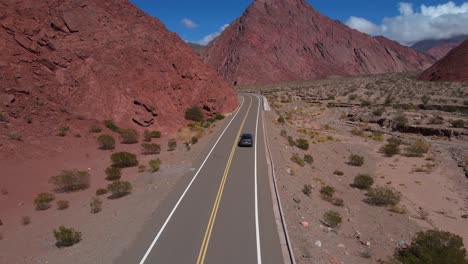 Drone-shot-following-a-gray-car-driving-through-the-Quebrada-las-Angosturas-in-Catamarca,-Argentina-on-a-curvy-road