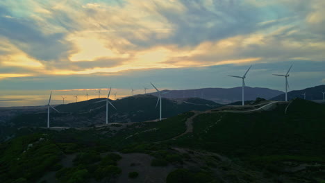 Vista-Aérea-Del-Parque-Eólico-Con-Turbinas-Eólicas-Giratorias-Para-Producir-Electricidad-Y-Energía-Sostenible-Para-La-Población-En-España-Málaga-Durante-Una-Hermosa-Puesta-De-Sol