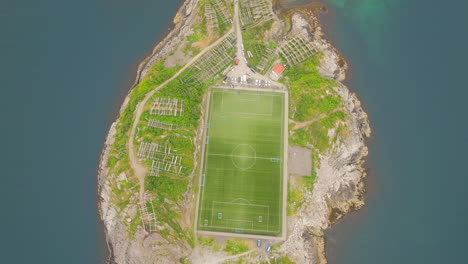 Cod-drying-racks-next-to-famous-Henningsvaer-football-pitch,-Lofoten,-aerial