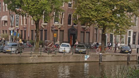 Gruppe-Von-Touristen-Auf-Fahrrädern,-Die-Entlang-Des-Kanals-In-Amsterdam,-Niederlande,-Radeln
