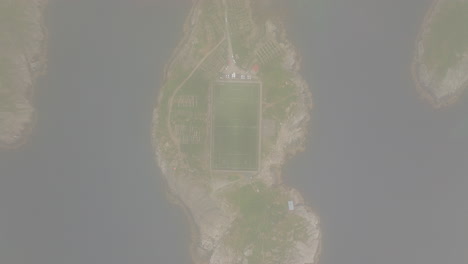 Drone-descends-through-clouds-to-reveal-iconic-Henningsvaer-soccer-field,-Norway