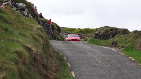 Coche-De-Rally-Irlanda-Estrecha-Carretera-De-Montaña-Con-Gente-Tomando-Fotos-En-West-Cork,-Irlanda