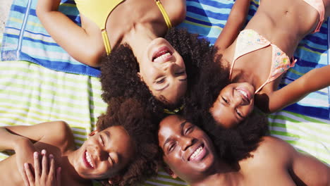 Portrait-of-african-american-parents-and-two-children-lying-on-a-towel-at-the-beach-smiling