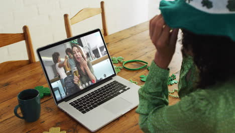 Caucasian-woman-on-laptop-video-call-celebrating-st-patrick's-day-with-friends