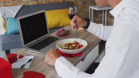Caucasian-man-making-video-call-using-laptop-eating-meal-and-drinking-wine