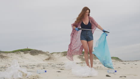 Kaukasische-Frau-Mit-Latexhandschuhen,-Die-Mit-Einem-Greiferstock-Müll-Vom-Strand-Sammelt