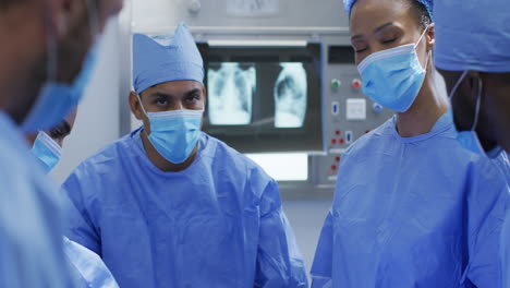 Mixed-race-surgeons-wearing-protective-clothing-discussing-in-operating-theatre