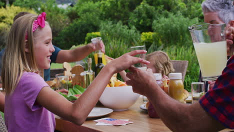 Smiling-caucasian-girl-drinking-lemonade-at-family-celebration-meal-in-garden