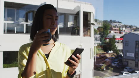 Mixed-race-gender-fluid-person-drinking-cup-of-coffee-and-using-smartphone-on-roof-terrace