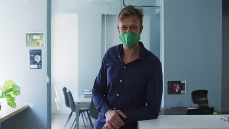 Portrait-of-caucasian-man-wearing-face-mask-standing-in-modern-office