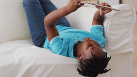 African-american-boy-smiling-while-using-digital-tablet-while-lying-on-the-couch-at-home