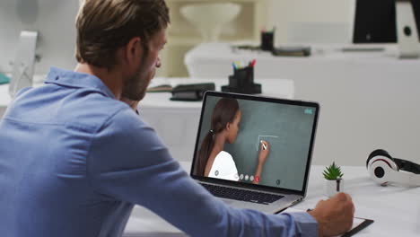 Caucasian-male-student-using-laptop-on-video-call-with-female-teacher,-making-notes