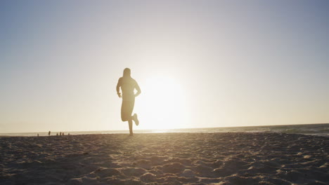 African-american-man-running-on-beach,-exercising-outdoors-in-beach-in-the-evening