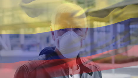 Animation-of-flag-of-colombia-waving-over-man-wearing-face-mask-during-covid-19-pandemic