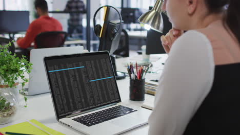 Caucasian-woman-sitting-at-desk-watching-coding-data-processing-on-laptop-screen