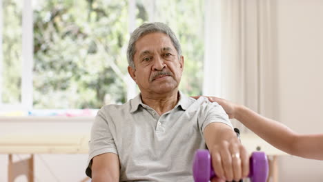 Diverse-male-physiotherapist-advising-and-senior-man-in-wheelchair-using-dumbbells,-in-slow-motion