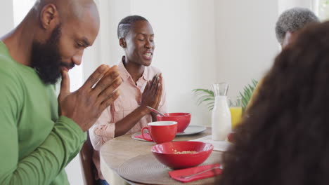 Video-of-happy-african-american-parents,-daughter-and-grandmother-saying-grace-at-dinner-table