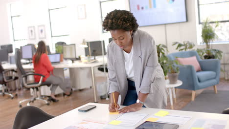 Mujer-De-Negocios-Informal-Afroamericana-Usando-Tableta-Y-Tomando-Notas-En-La-Oficina,-Cámara-Lenta