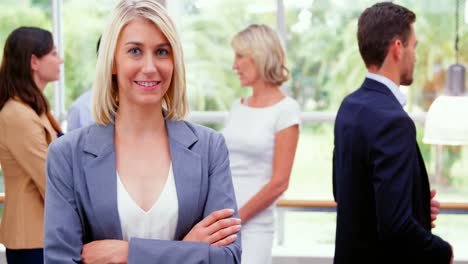 Female-business-executive-smiling-at-camera-while-colleagues-interacting-in-background