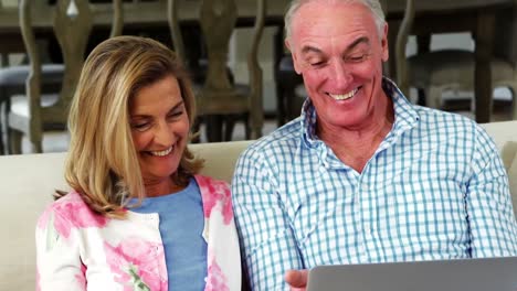 Smiling-senior-couple-using-laptop-in-living-room