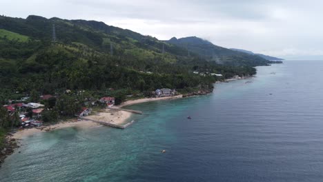 Filipino-coastal-seaside-houses-along-coastline-road-at-tropical-lush-green-overgrown-foothill-on-Cebu-island