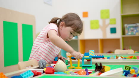 Süßes-3-jähriges-Kaukasisches-Mädchen,-Das-Mit-Plastikziegeln-Spielt-Und-Zu-Hause-Einen-Turm-Auf-Dem-Tisch-Baut