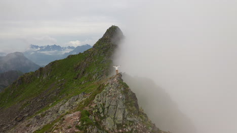 Revealing-drone-around-young-hiker-man-standing-on-Mountain-Peak-Summit,-Fløya-and-Djevelporten-above-Svolvær-in-Lofoten,-Norway,-aerial-footage