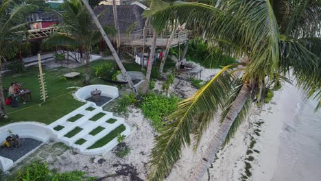 ShakaBrah-in-Siargao---Dolly-out-aerial-through-coconut-palm-trees-revealing-couple-cuddling-at-tropical-beach-resort