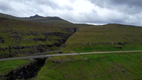 Faroe-Islands-green-volcanic-mountains-of-Eysturoy,-car-passing-by-on-road