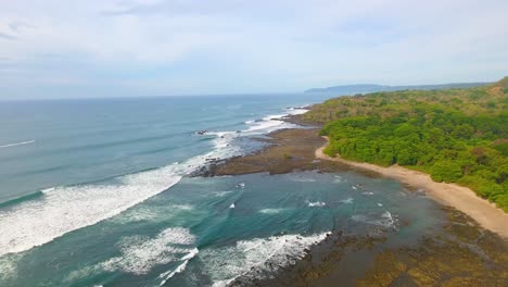 Pulling-back-from-the-coast-of-Costa-Rica-overlooking-the-shoreline-of-Piedra-Point-at-low-tide-with-rolling-waves-approaching-shore