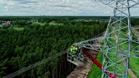 Luftaufnahme-Von-Elektrikern-An-Einem-Strommast-Auf-Einer-Hubarbeitsbühne-Oder-Einem-Hubarbeitsbühnengerät,-Während-Sie-Die-Stromleitungen-Reparieren-Und-Gefährliche-Arbeiten-Mit-Blick-Auf-Den-Wald-Ausführen