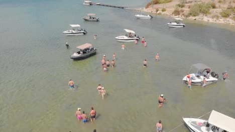 Drohnengruppe-Menschen-Verlassen-Den-Strand,-Um-In-Freizeitboote-Zu-Steigen,-Sommerlich-Sonniges-Blaues-Wasser