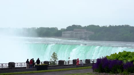 Statische-Weitwinkelaufnahme-Der-Wunderschönen-Niagarafälle-In-Der-Kanadischen-Provinz-Ontario-Mit-Blick-Auf-Den-Riesigen-Wasserfall-Und-Fußgänger-Oder-Touristen-Auf-Dem-Geländer-Der-Sehenswürdigkeit-In-Zeitlupe