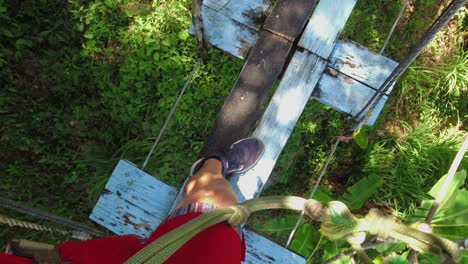 POV:-Feet-on-skywalk,-man-walks-on-bridge-high-in-jungle-tree-canopy