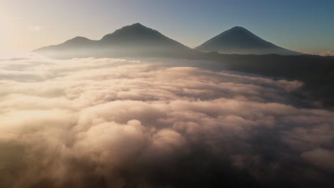 Flying-over-a-foggy-valley-with-Volcanic-mountain-background,-sunrise-in-Bali---Aerial-view