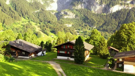 Swiss-timbered-Chalet-houses-on-green-hill-overlooking-snow-capped-Grindelwald-alps-mountain-peaks