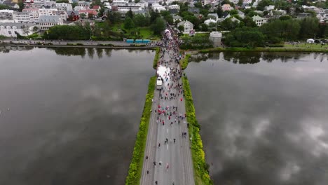Reykjavik-marathon-people-crossing-Tjörnin-lake-in-capital-city,-aerial