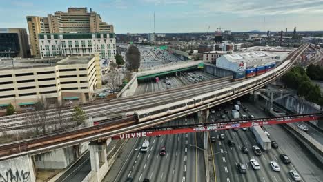 Aerial-view-of-train-riding-on-rail-and-cars-driving-on-busy-highway-in-Atlanta-City,-USA