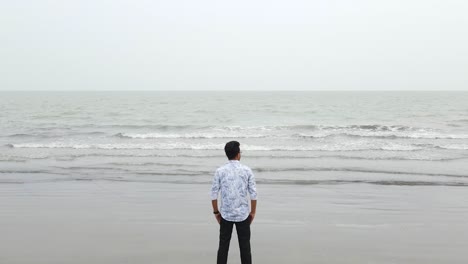 Ascending-aerial-view-of-a-solitary-man-staring-at-the-ocean-in-slow-motion