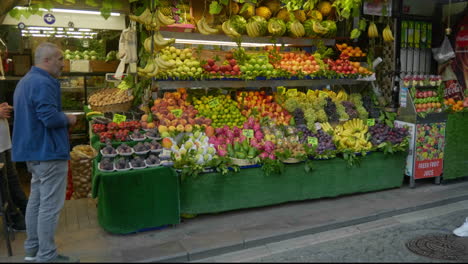 Vendor-of-fresh-fruit-and-vegetables-stands-by-his-colourful-market-stall