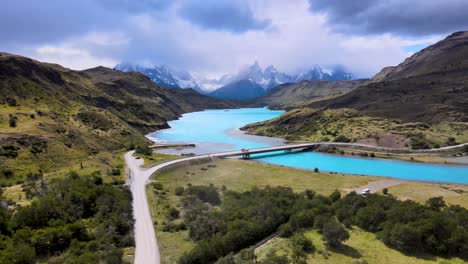 Drone-flight-in-Patagonia,-Chile-and-Argentina,-with-views-of-crystal-blue-waters-and-snow-covered-mountains-and-a-bridge-connecting-mountain-landscapes