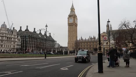 Klassisches-Schwarzes-Londoner-Taxi-Mit-Dem-Ikonischen-Big-Ben-Und-Dem-Parliament-Square-Im-Hintergrund